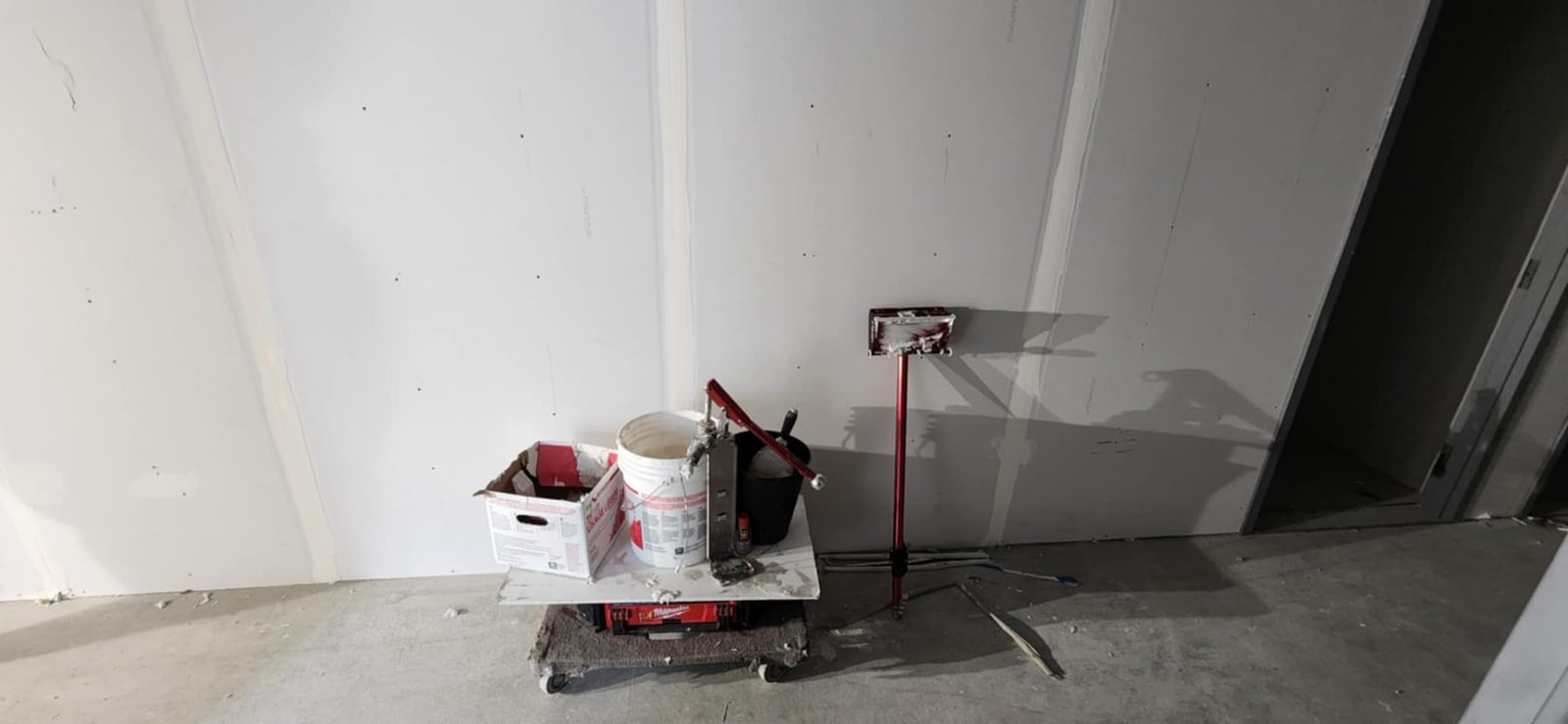 Drywall wall with visible taped seams beside joint compound buckets and finishing tools