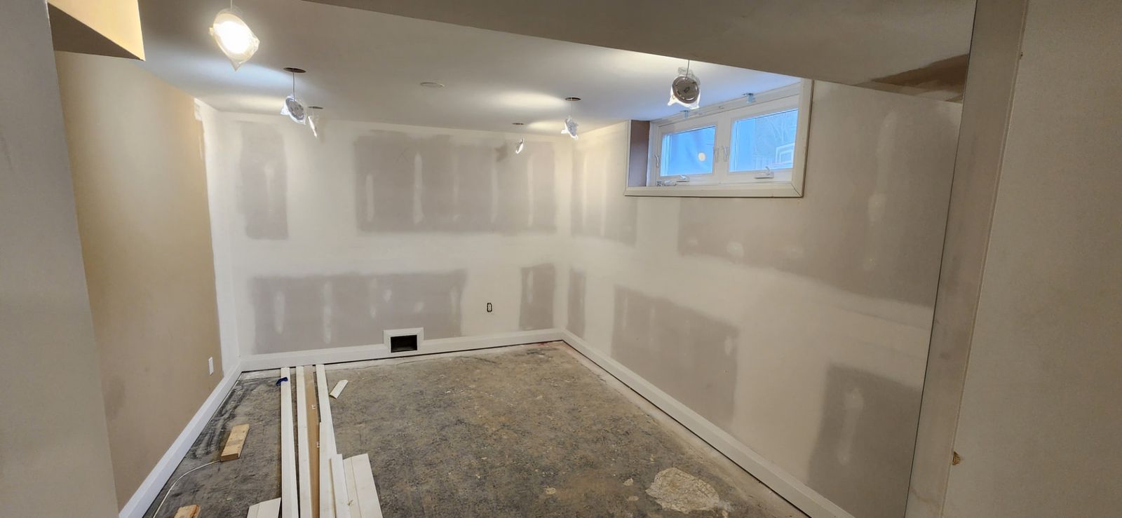 After: Basement bedroom with taped drywall seams, new baseboards and trim boards staged on the floor