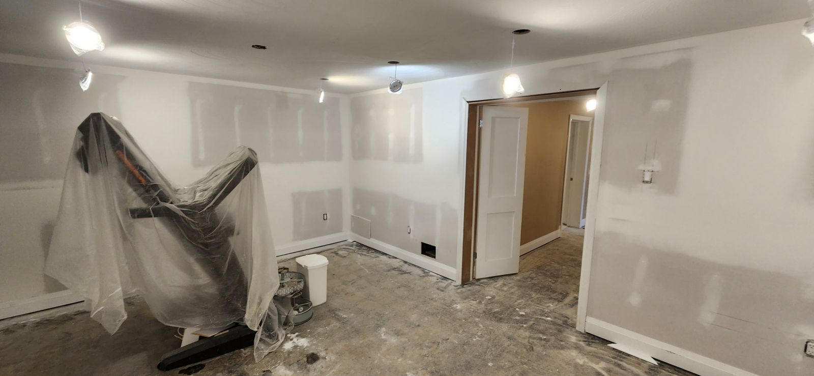 After: Basement living area with finished drywall, new white doors and equipment covered in protective sheeting