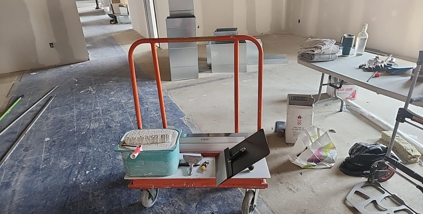 Drywall finishing tools and joint compound on a trolley in front of taped commercial partitions