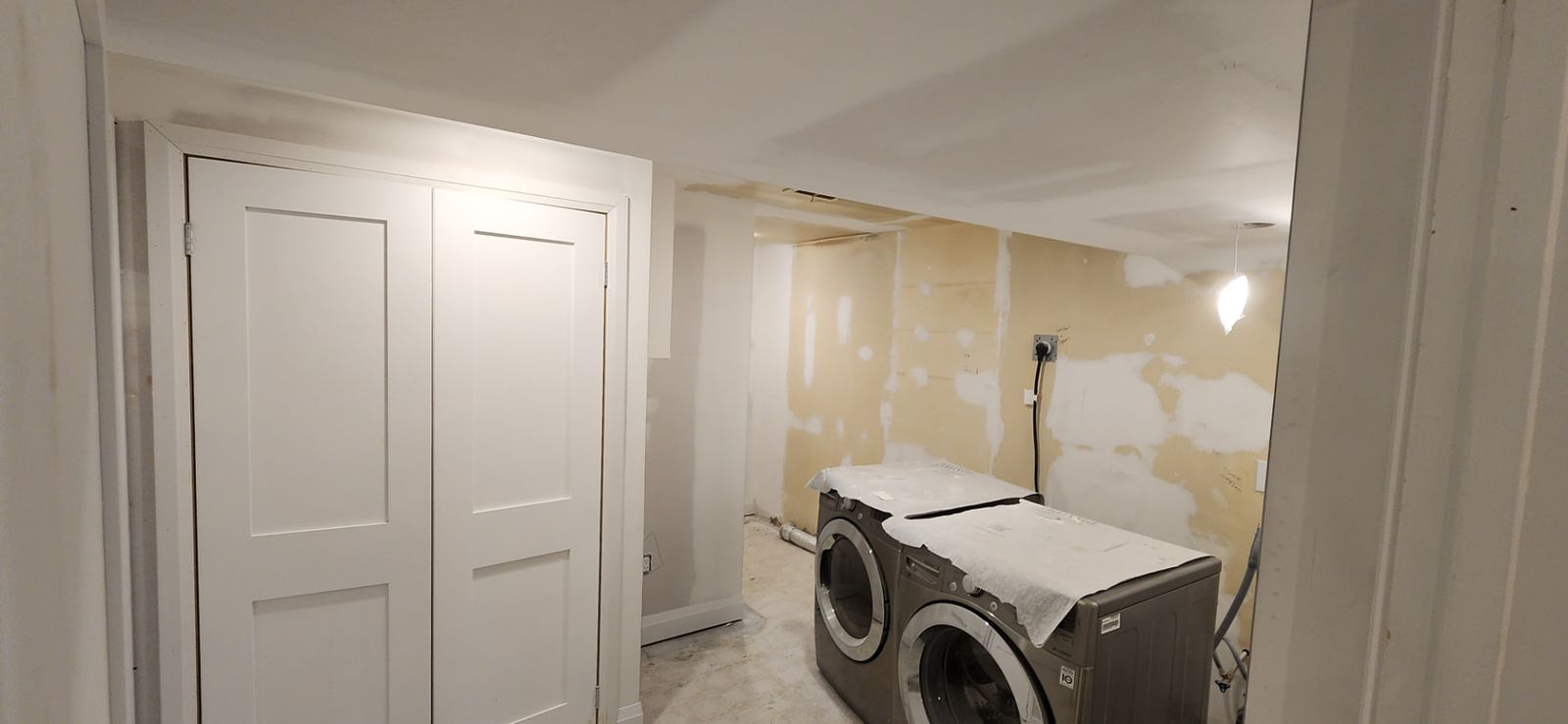 After: Laundry hallway with new white double doors and patched plaster walls beside protected washer and dryer