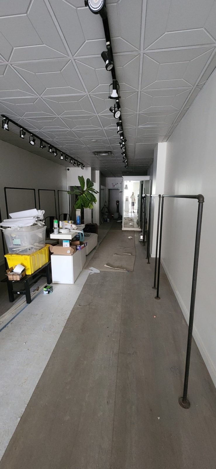 Long retail interior with smooth walls, geometric ceiling panels and track lighting during renovation