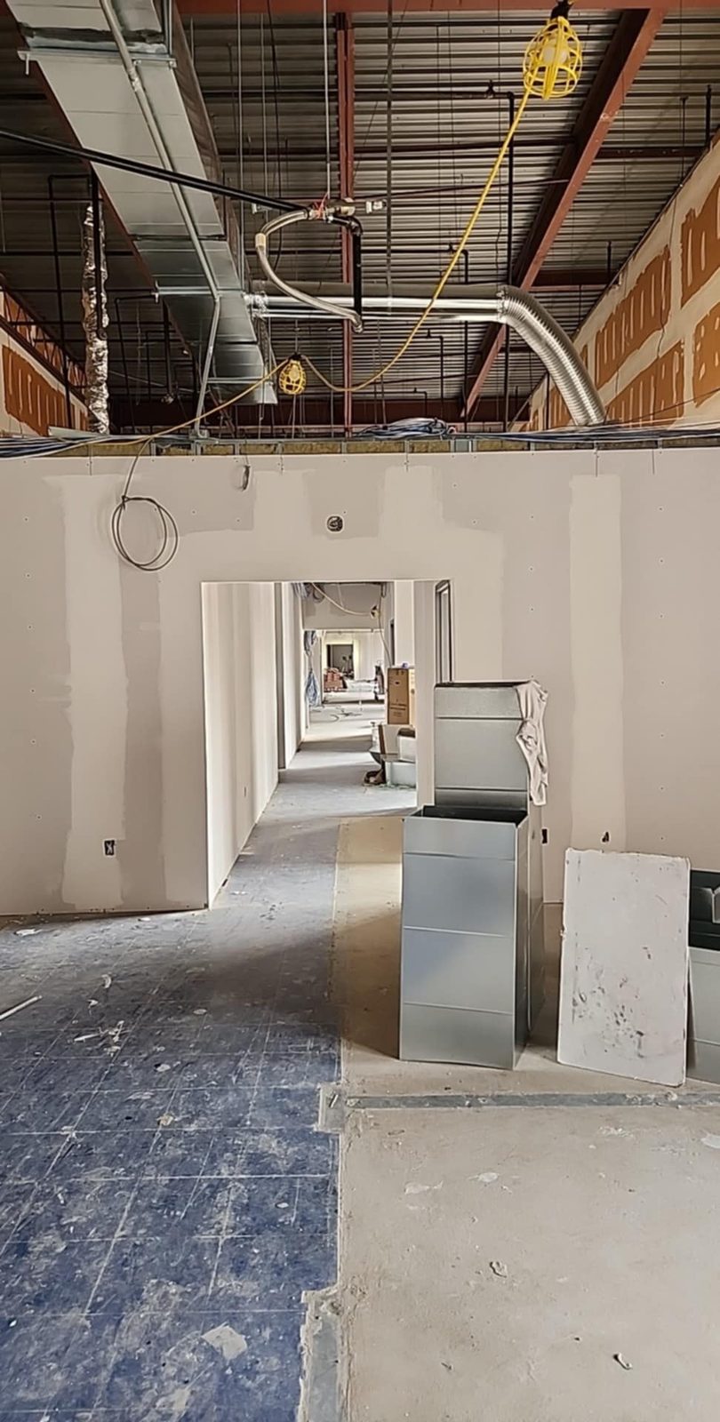 Taped drywall doorway and corridor beneath exposed steel beams and ventilation ducts