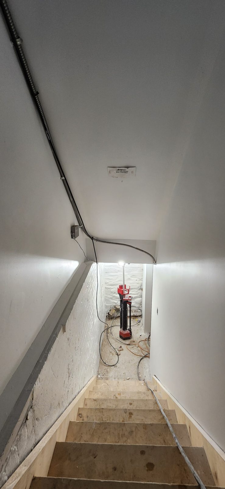 Stairwell with smooth finished walls and ceiling, exposed conduit and a work light at the bottom